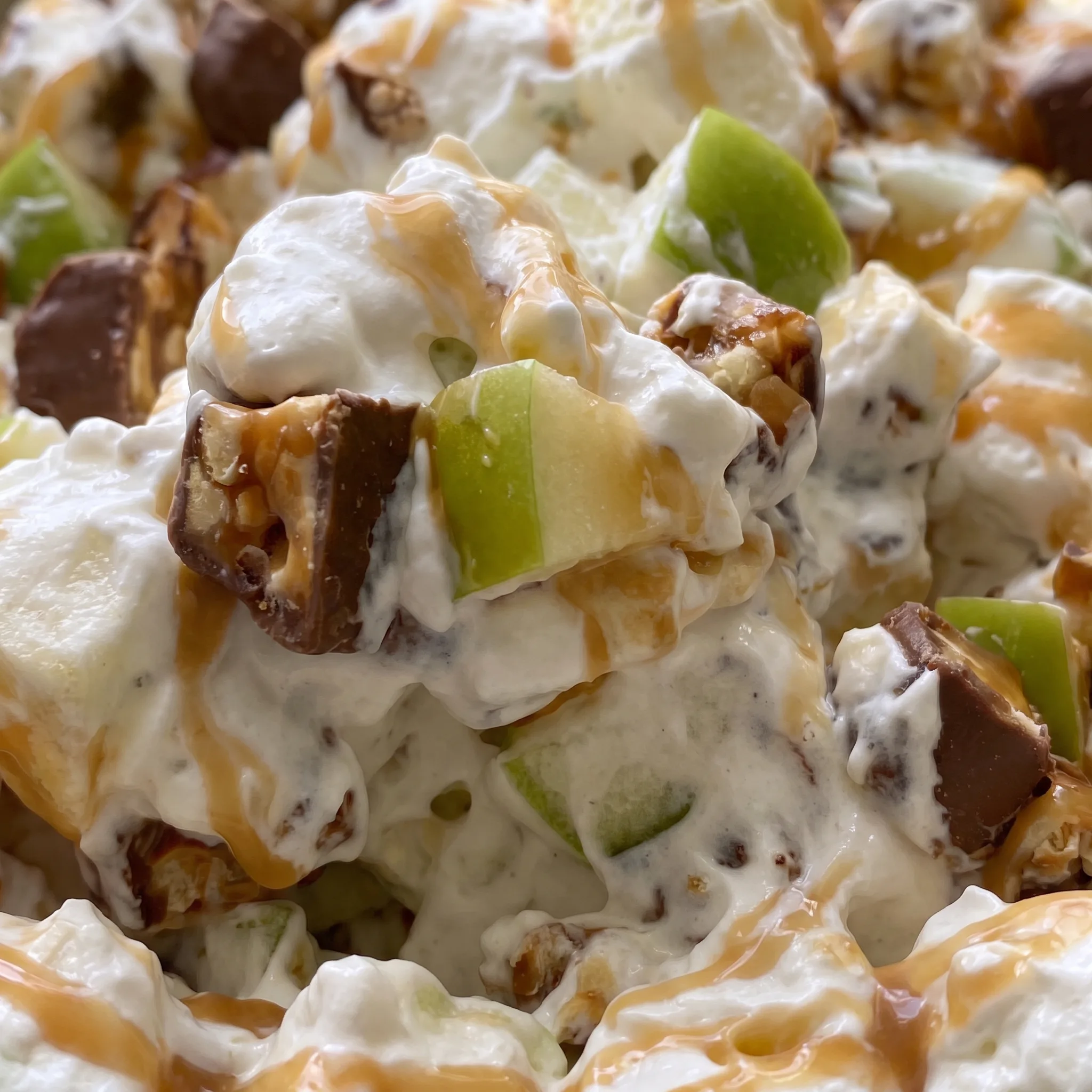 Creamy whipped topping with caramel swirls, green apple chunks, and Snickers pieces in a dessert salad.