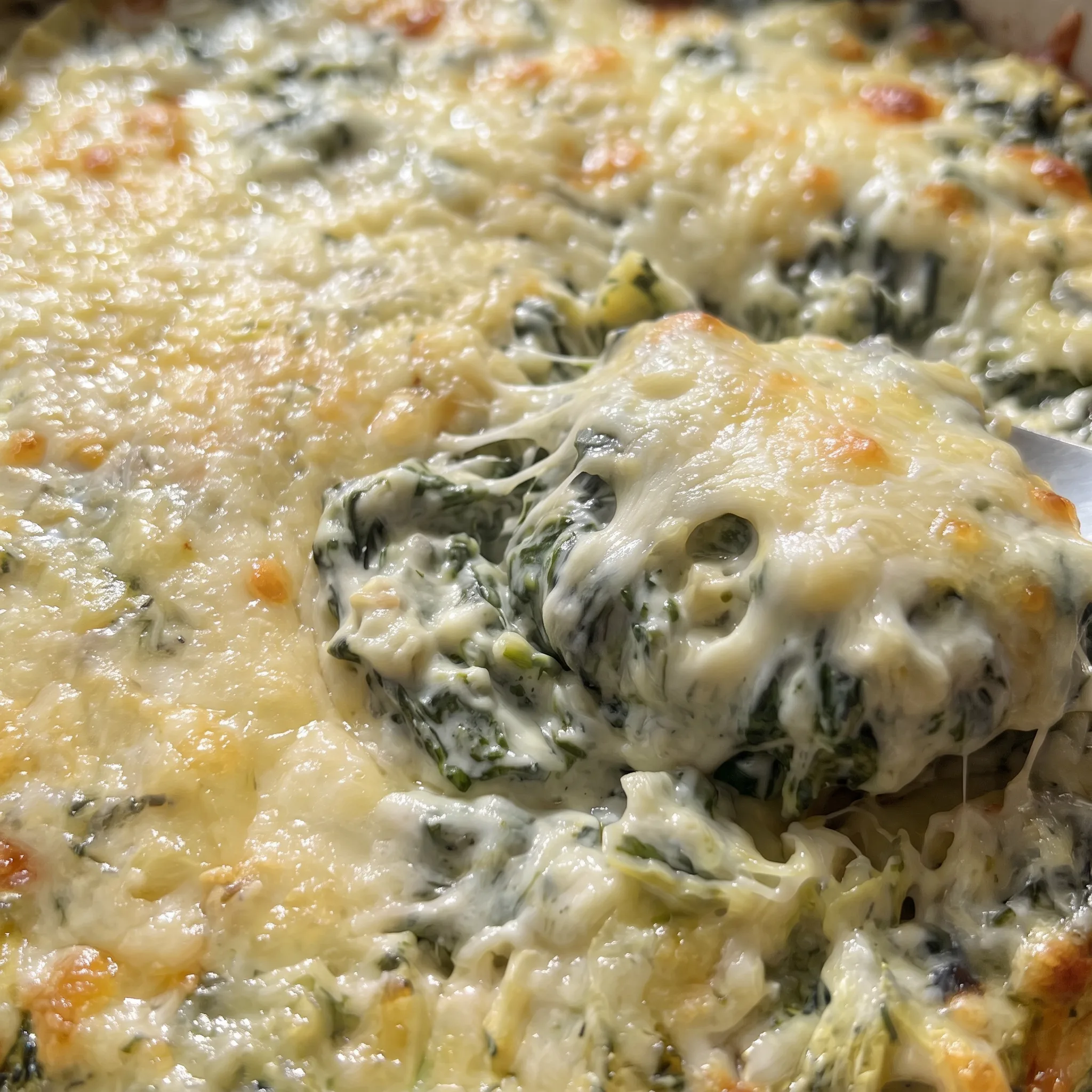Golden melted cheese pull over creamy dip with green spinach flecks and pale artichoke heart chunks.