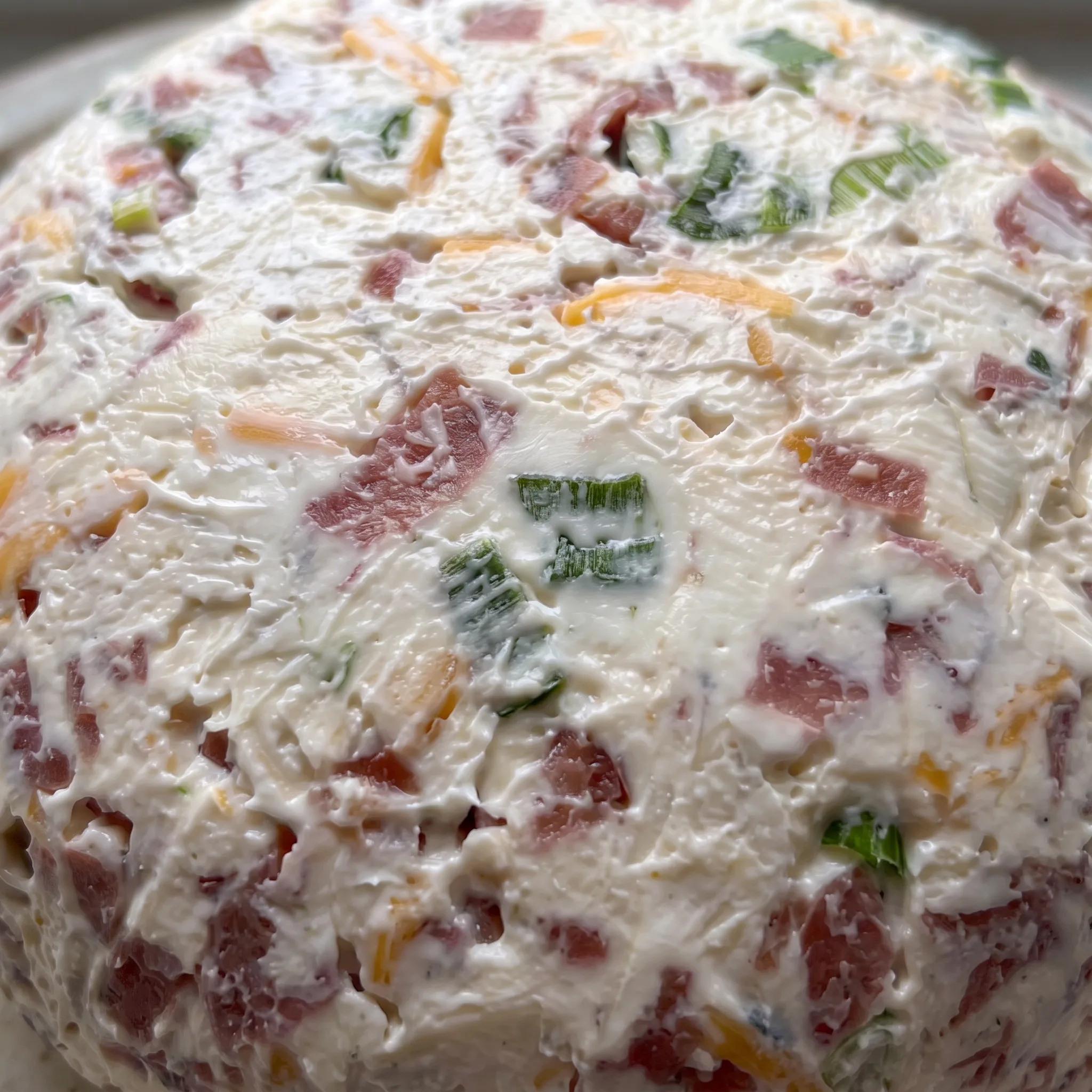 Creamy cheese ball surface speckled with green onion bits and shredded cheddar, edged with dried beef.