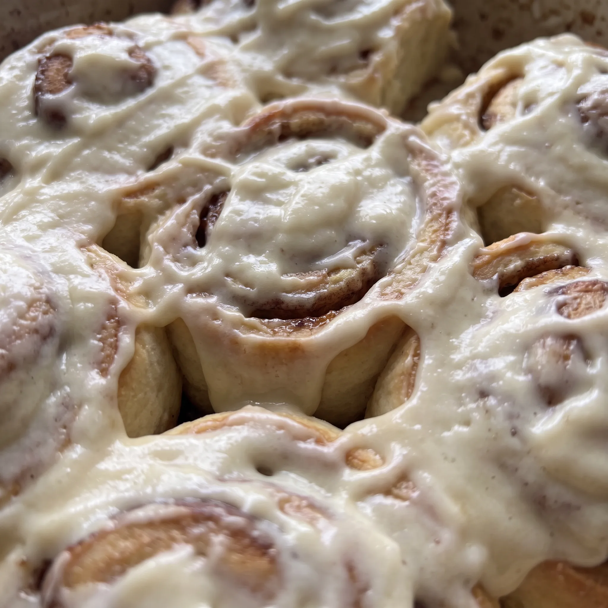 Thick cream cheese frosting spread over a golden cinnamon roll, with dark cinnamon and brown sugar swirls visible.