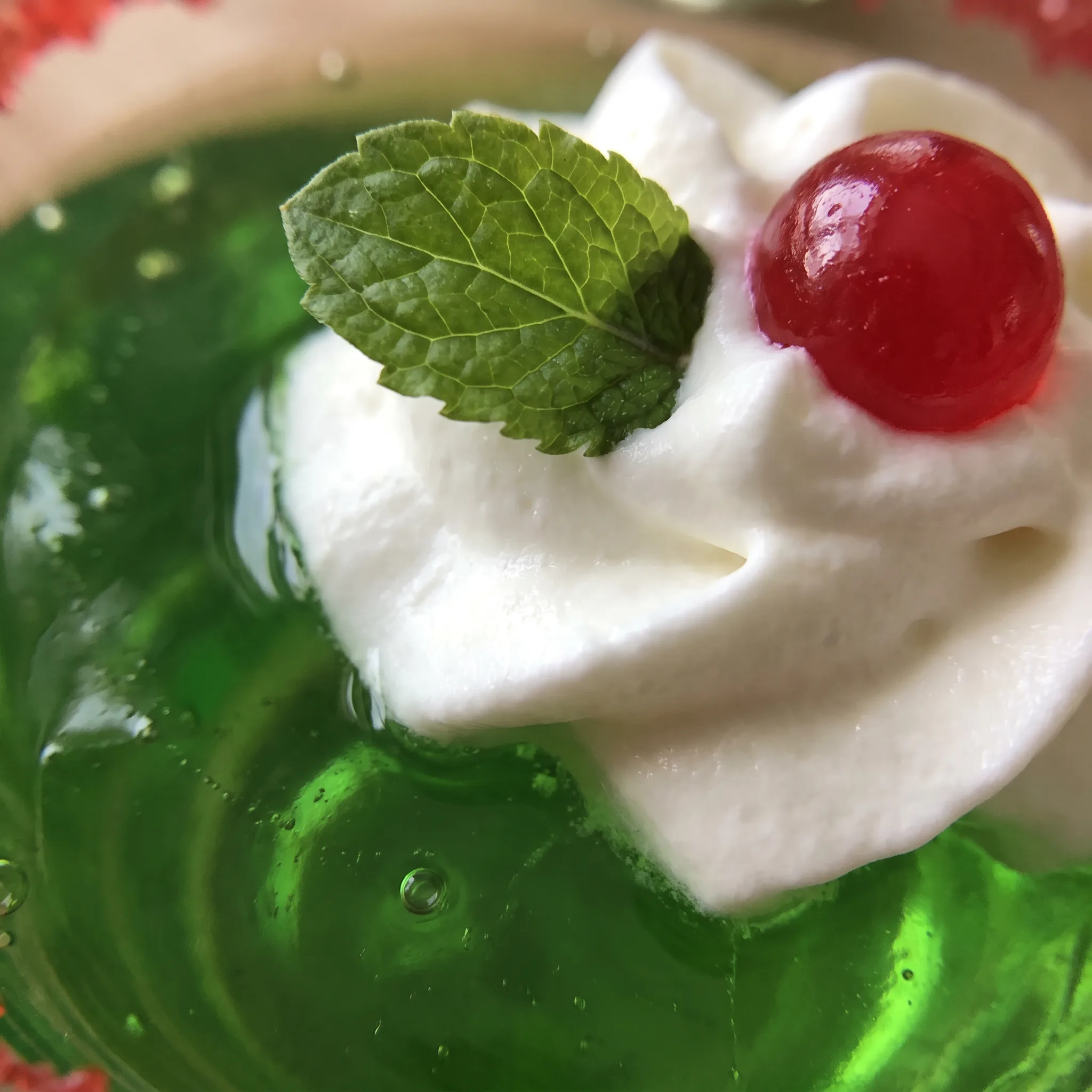 Glossy lime gelatin with a swirl of whipped cream, a mint leaf, and a red hot coated in red sanding sugar.