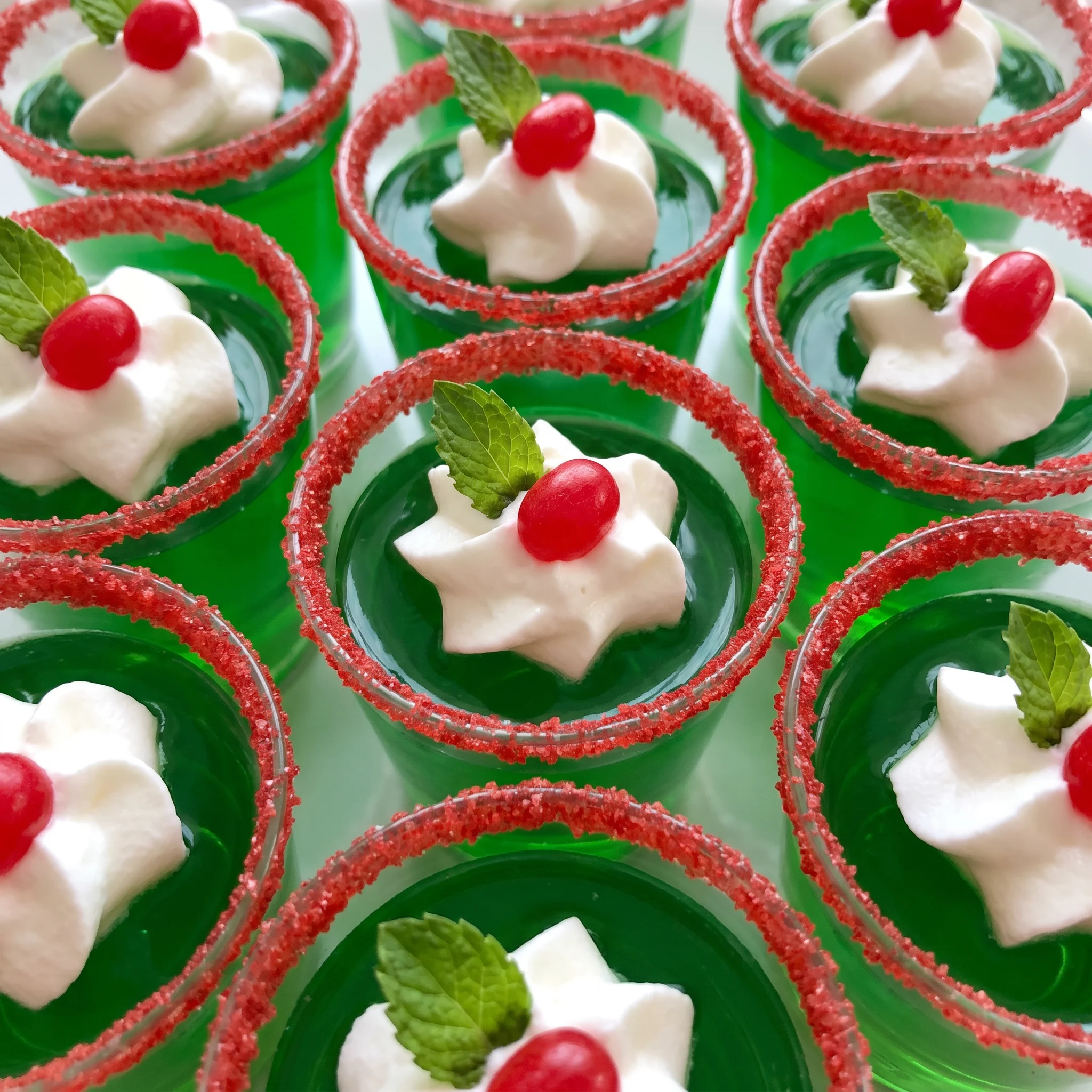 Lime gelatin shots topped with whipped cream, mint leaves, red hots, and red sanding sugar.