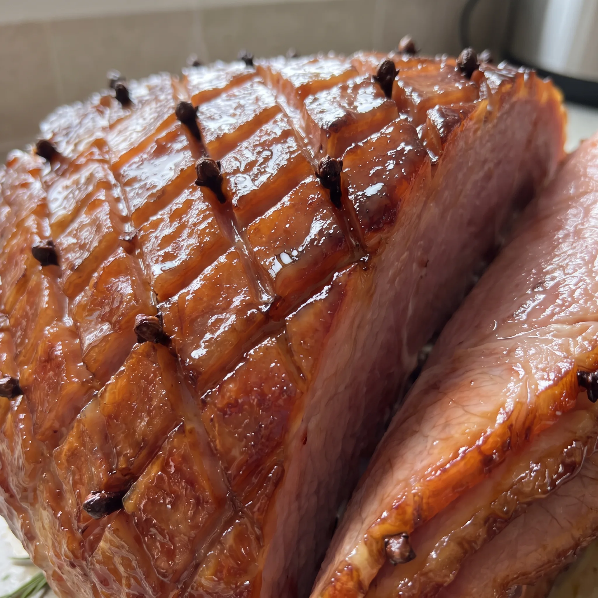 Sticky honey glaze over ham, dark whole cloves studded in, shiny surface with caramelized edges.