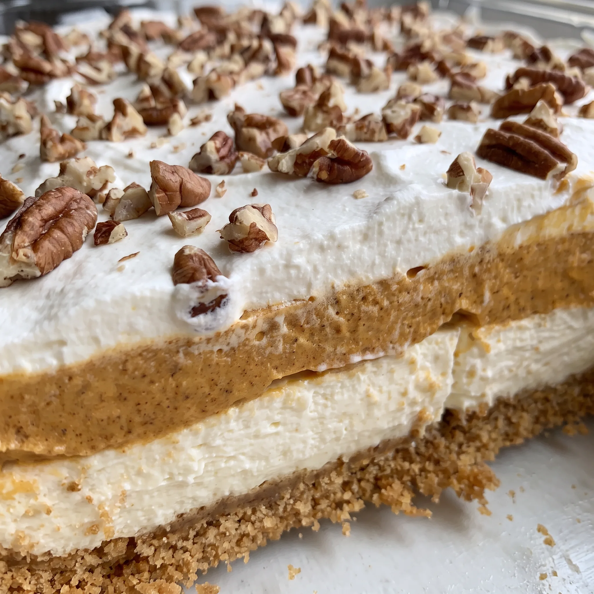 Creamy pumpkin and cream cheese layers on a graham cracker crust, topped with whipped topping and chopped pecans.