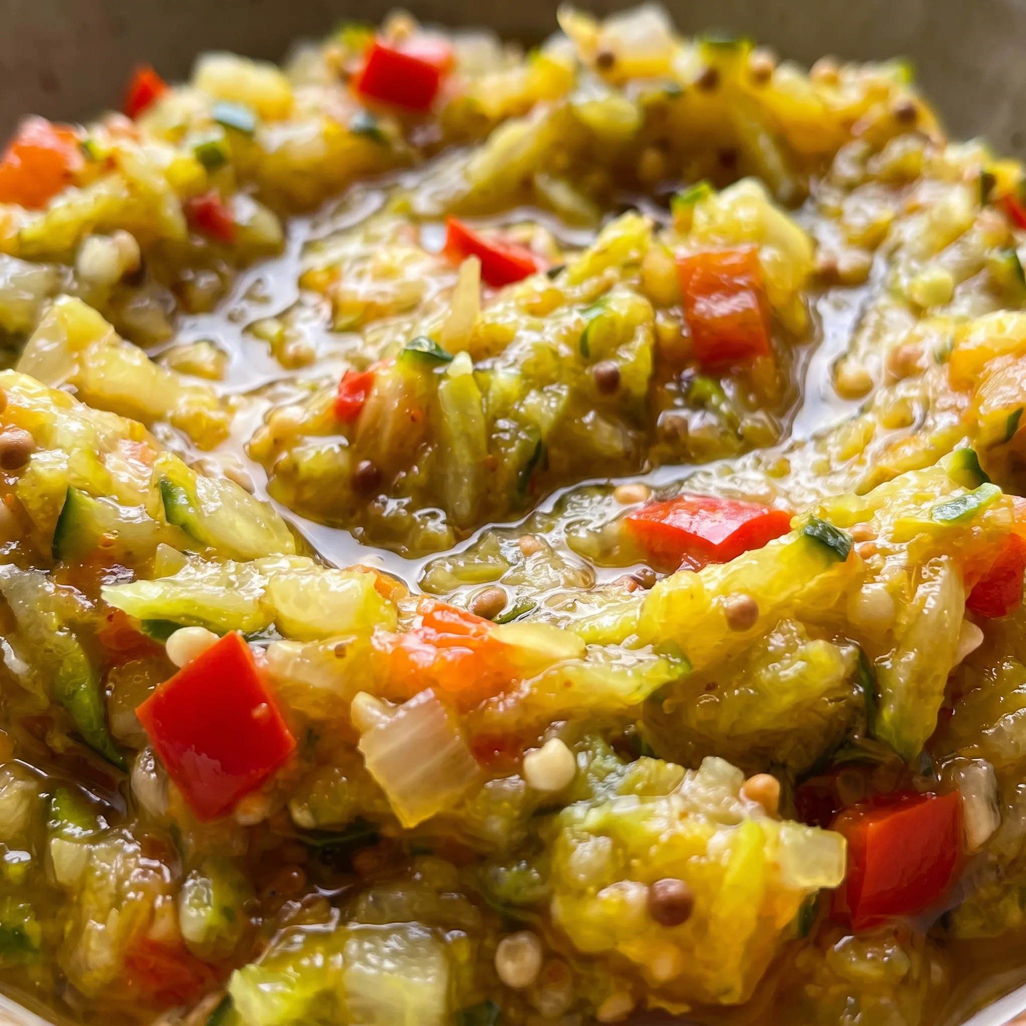 Glossy, finely chopped zucchini relish with soft onion bits and red bell pepper flecks, showing a moist, textured consistency.