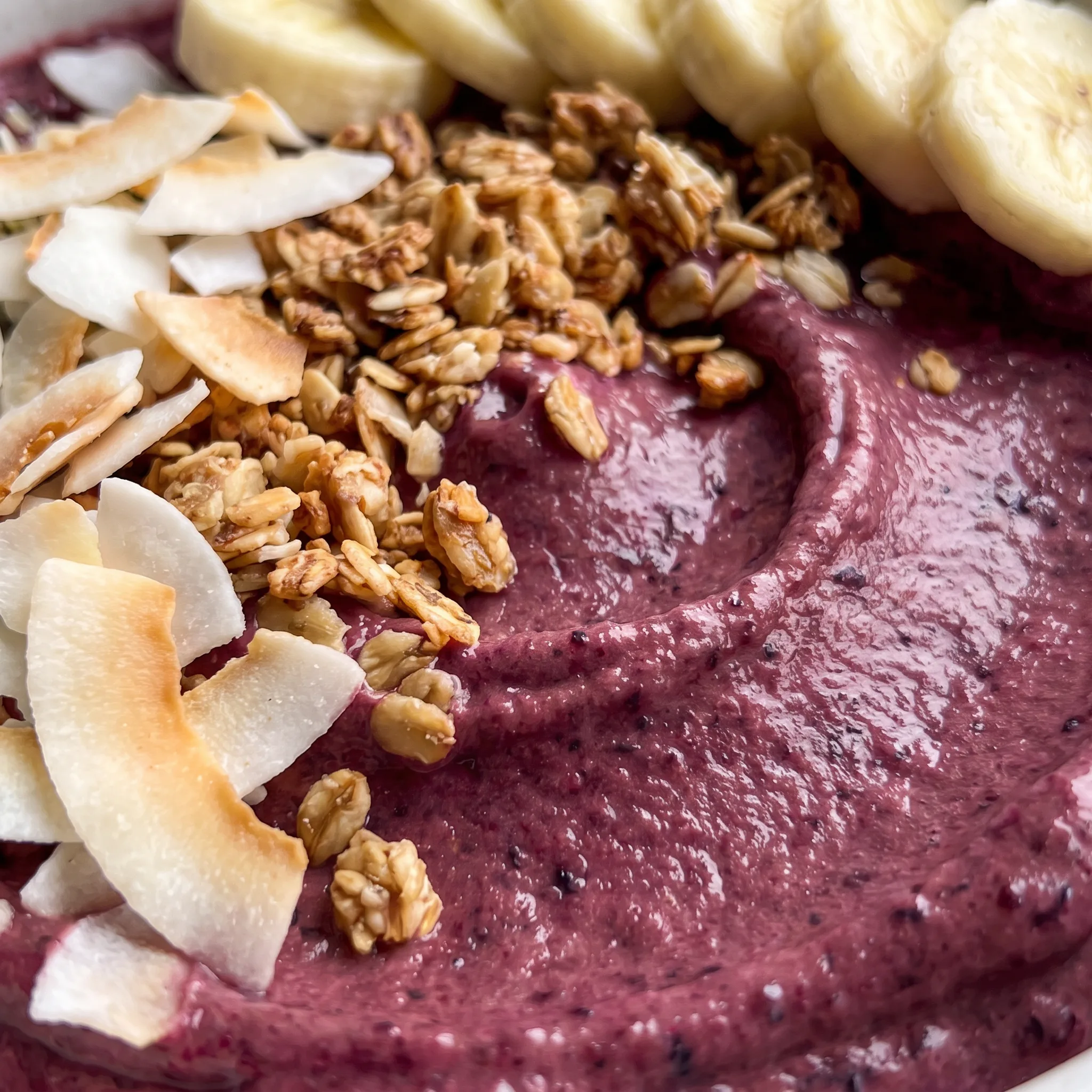Creamy blended berries with visible banana rounds and thick Greek yogurt, deep purple with pale swirls.