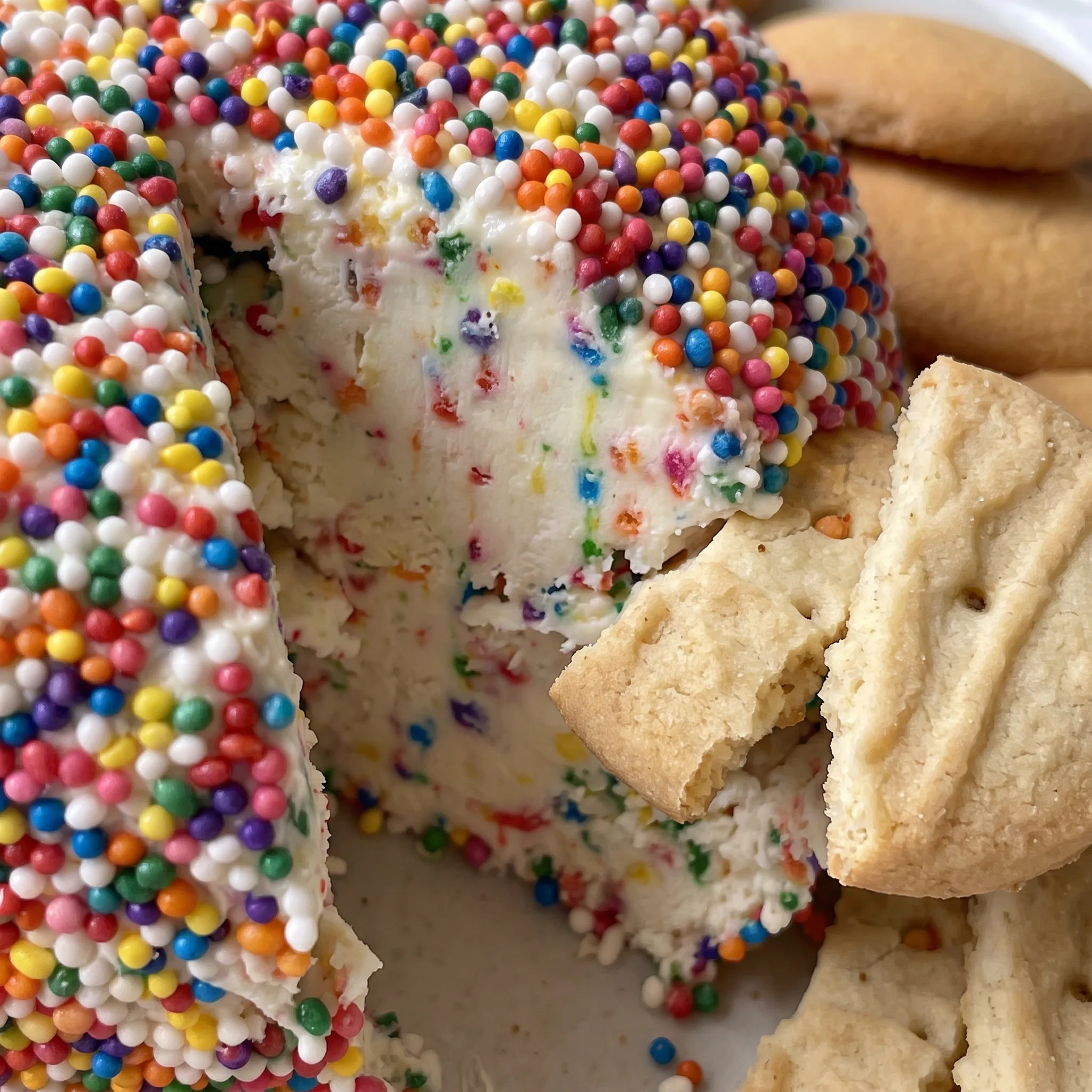 Rainbow sprinkles cover the creamy surface of a sweet cheese ball dotted with funfetti cake mix.