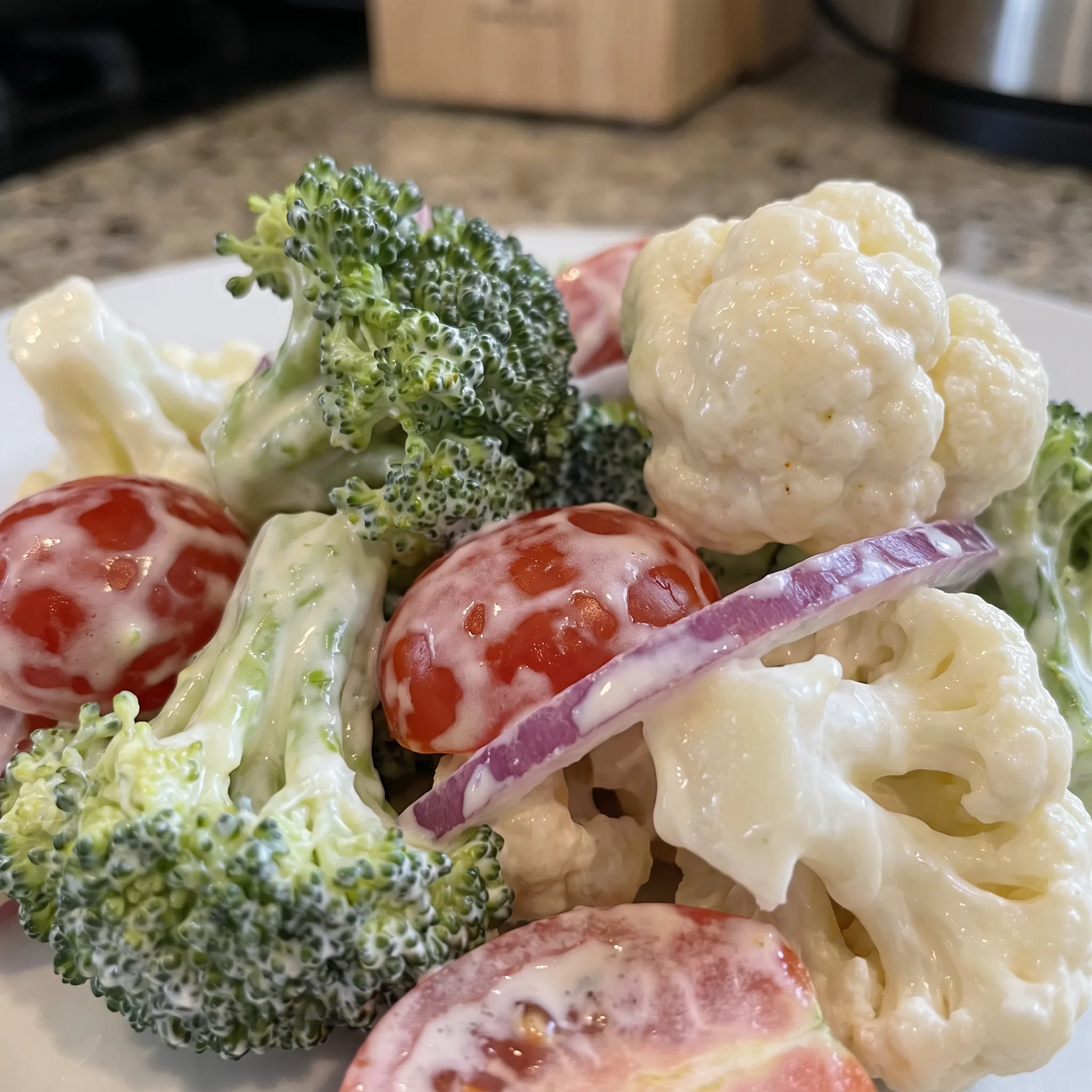 Crisp broccoli and cauliflower florets coated in creamy white dressing with halved red cherry tomatoes.