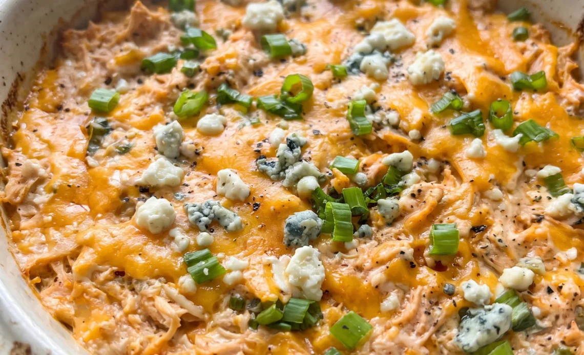 Buffalo chicken dip with shredded chicken in orange hot sauce, melted cheddar, green onion slices, and blue cheese crumbles.