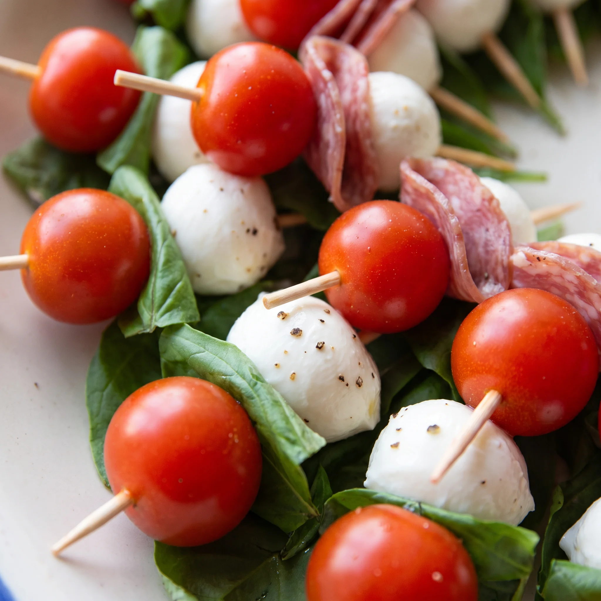 Glossy balsamic glaze beading on a mozzarella ball beside a halved grape tomato and a basil leaf.
