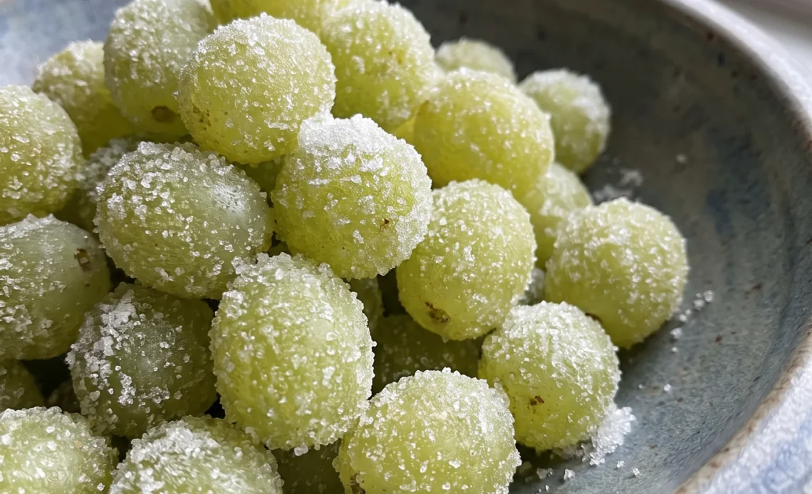 Champagne grapes coated in sugar, pale green and translucent, piled loosely with a glossy syrup sheen.