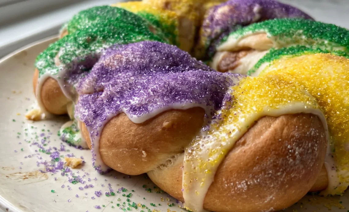 King cake ring with cream cheese filling, white frosting, and purple, green, and gold sugar bands.