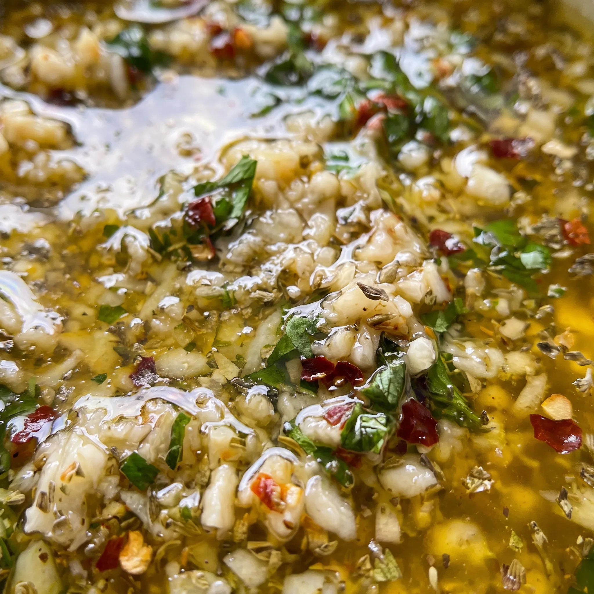 Golden olive oil pooling around bits of minced garlic, grated Parmesan and red pepper flakes, topped with green parsley.