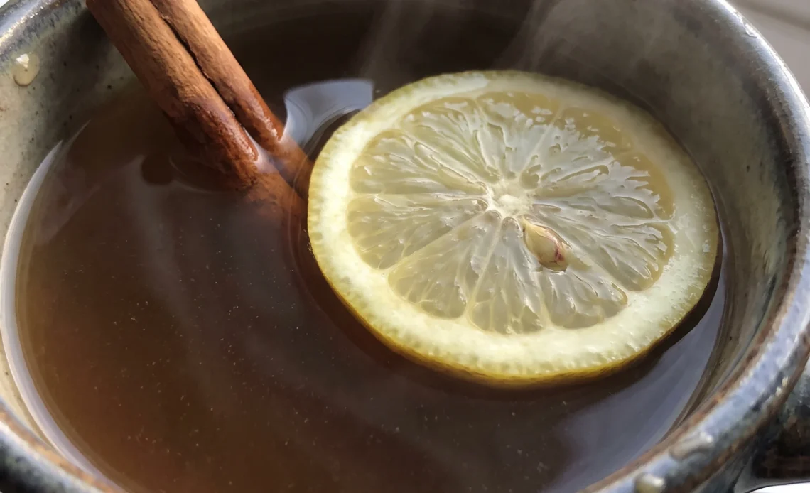 Hot toddy with tea, a lemon slice and a cinnamon stick in amber liquid.