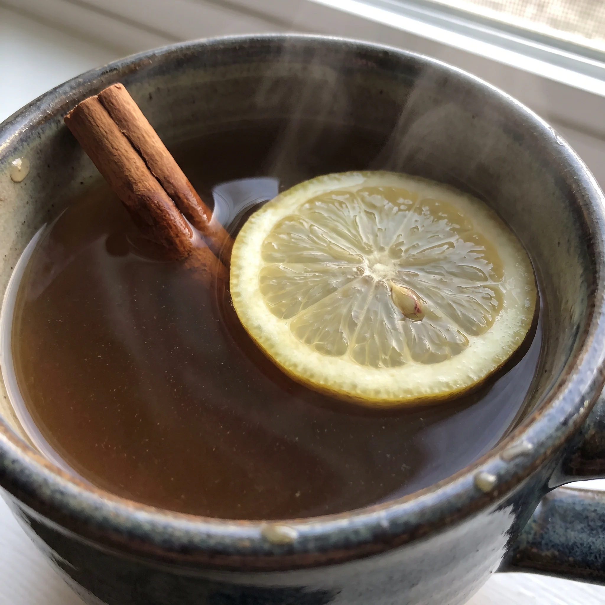 Hot toddy with tea, a lemon slice and a cinnamon stick in amber liquid.