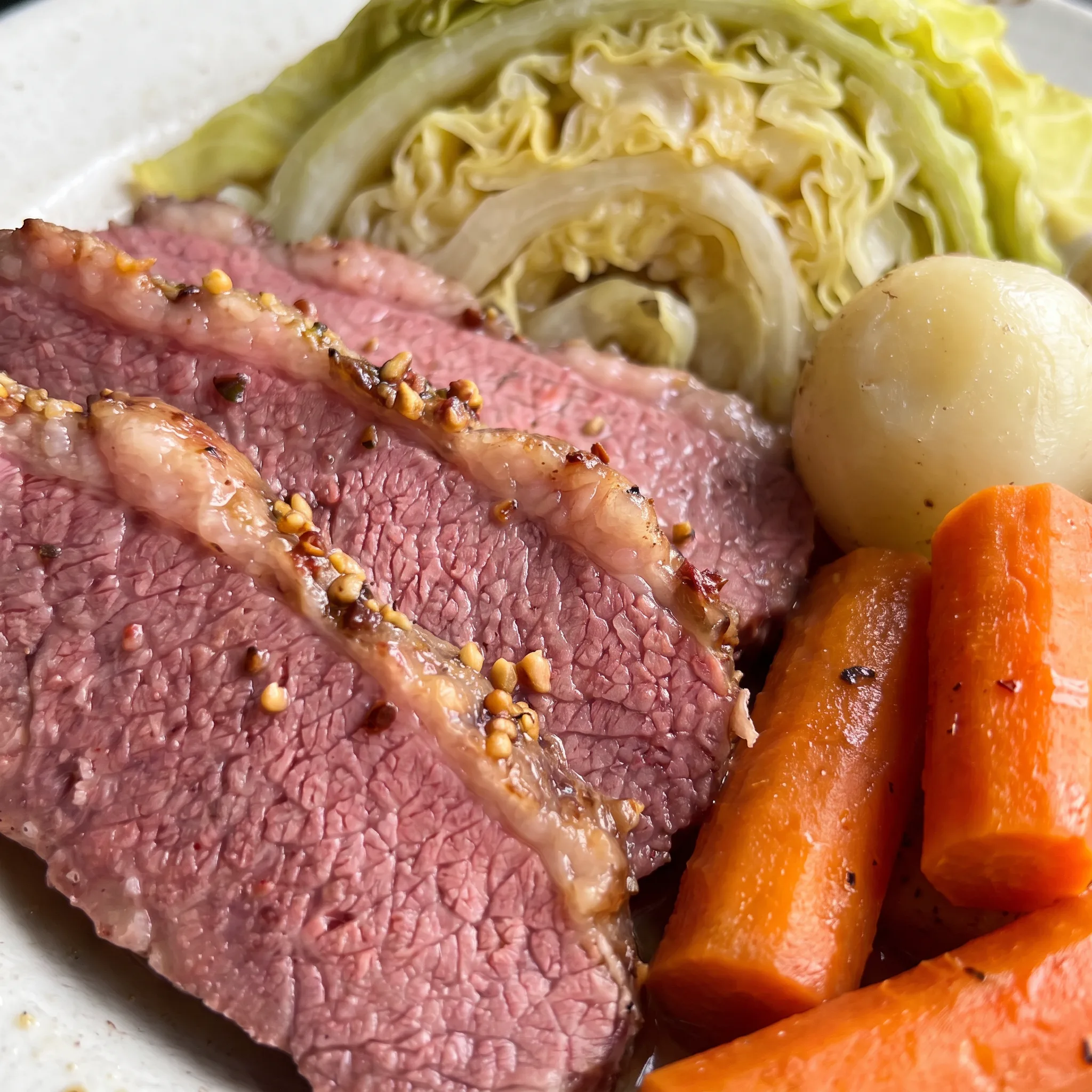 Slices of pink corned beef beside soft green cabbage, with tender orange carrot pieces and yellow potatoes.