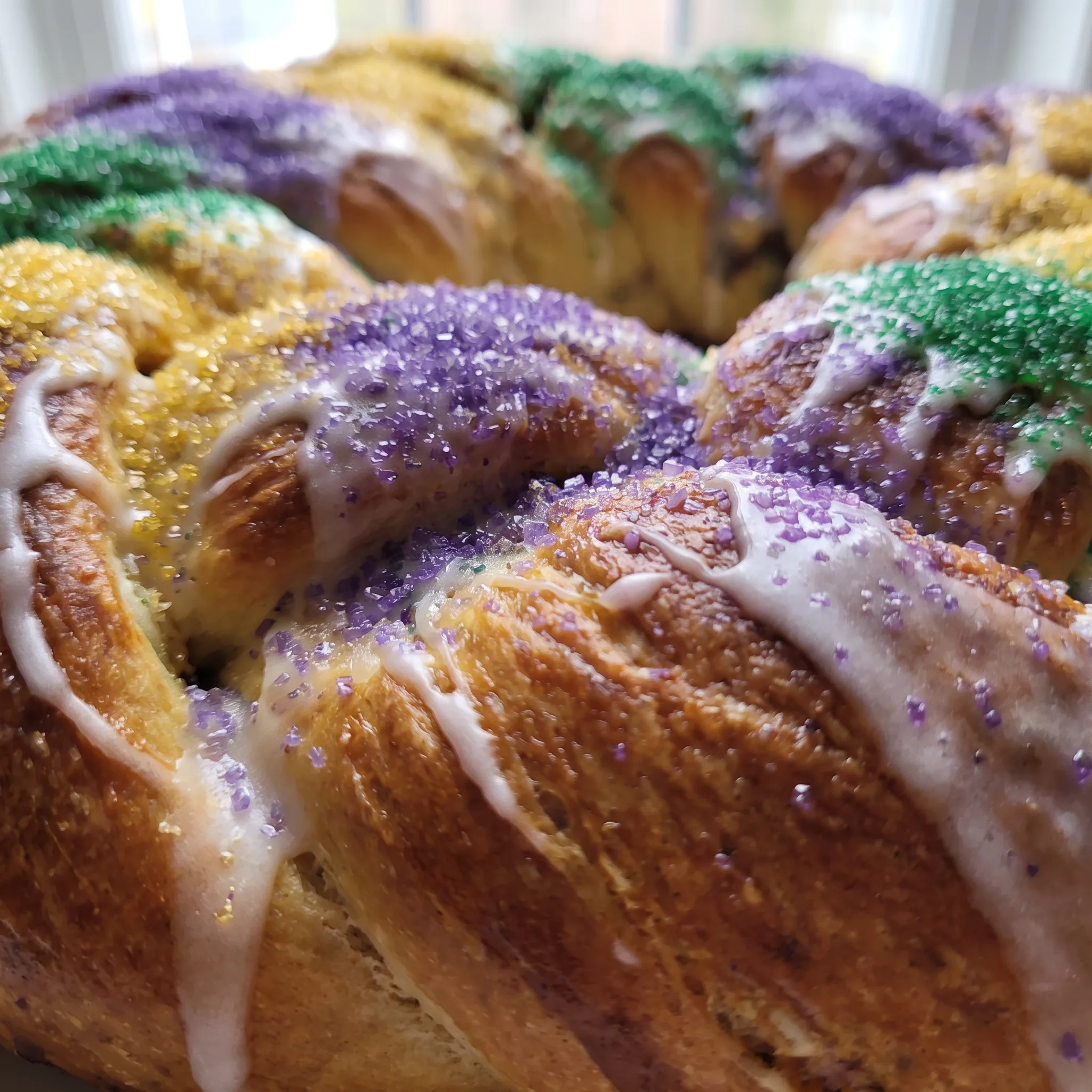 Iridescent purple, green, and gold sanding sugar crystals scattered across white frosting and golden cinnamon-swirled dough.