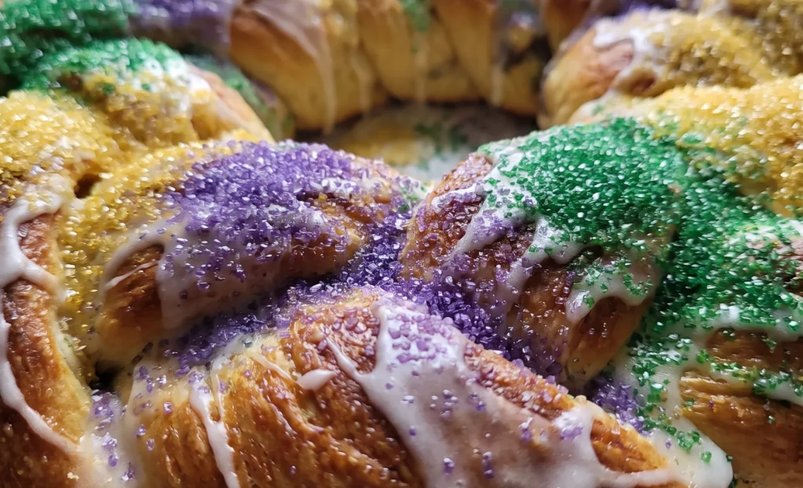 Mardi Gras king cake with cinnamon filling, frosting, and bands of purple, green, and gold sanding sugar.