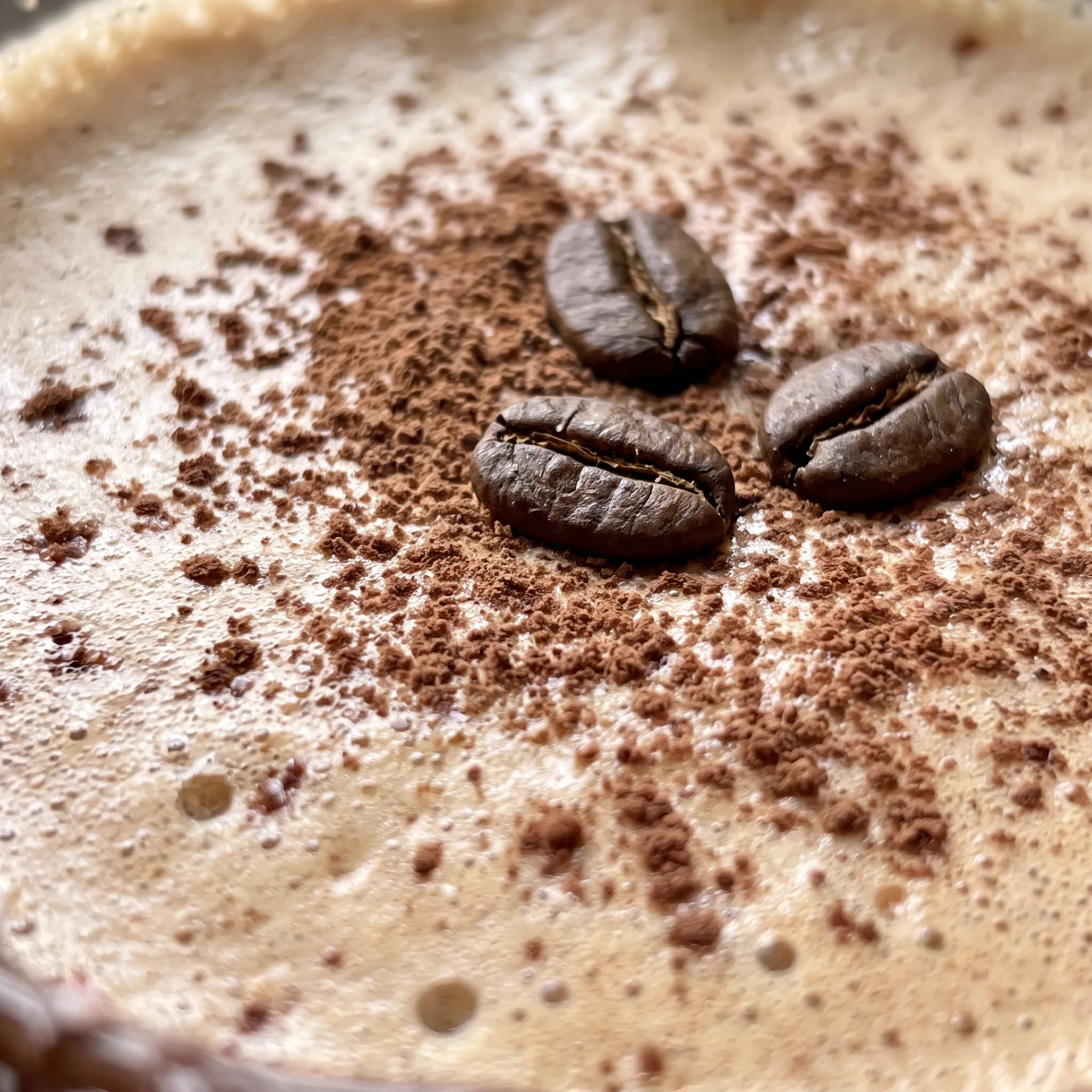 Creamy white foam layer over dark espresso martini, dusted with cocoa powder and crushed red and white peppermint pieces.