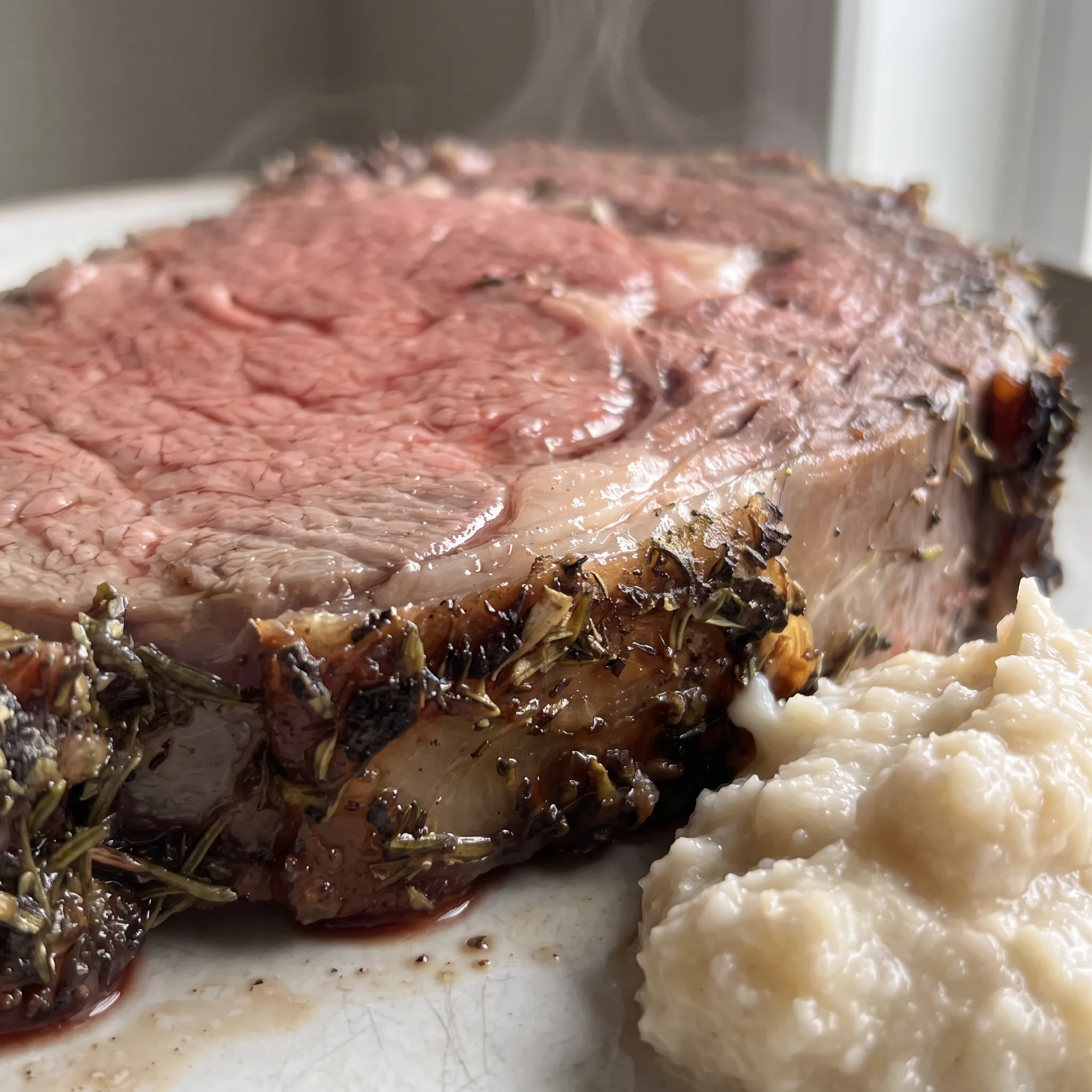 Sliced prime rib showing a pink center, dark crust, and melted butter with garlic and herb bits on the surface.