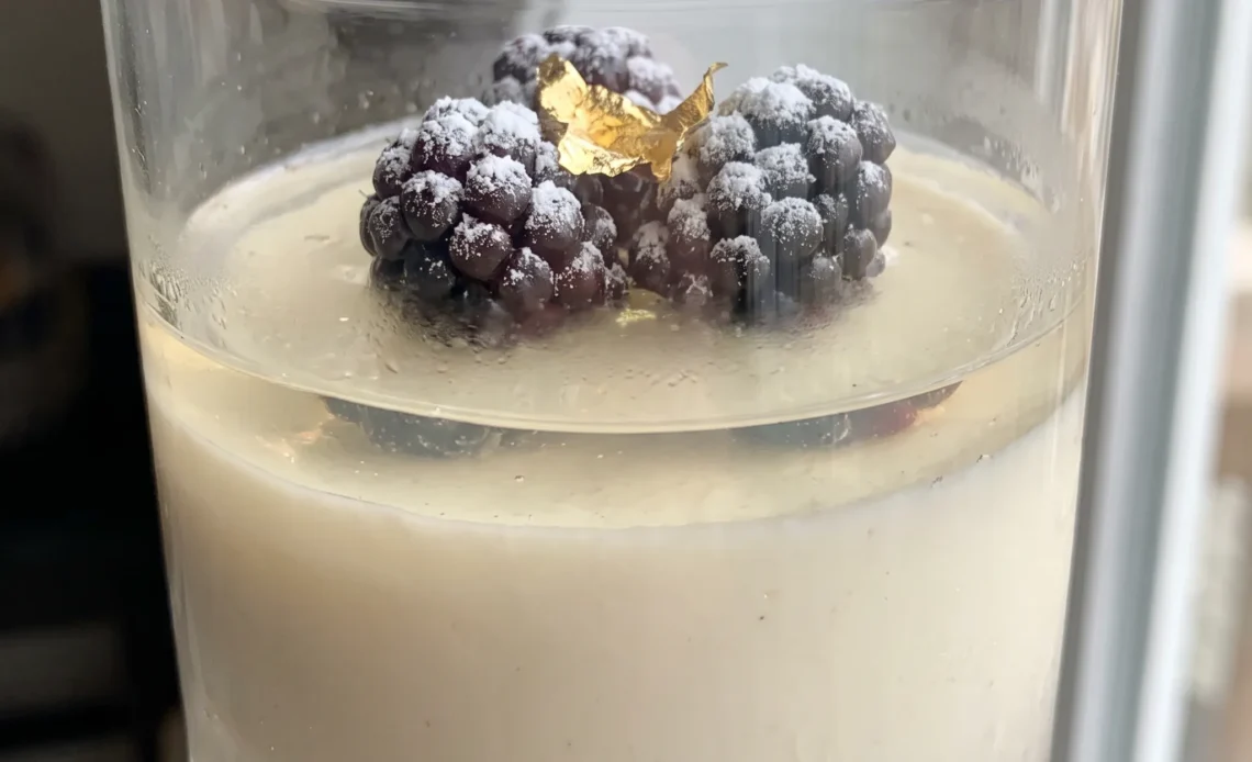 Sparkling wine panna cotta topped with fresh raspberries and blackberries, pale cream custard with glossy red and dark purple fruit.