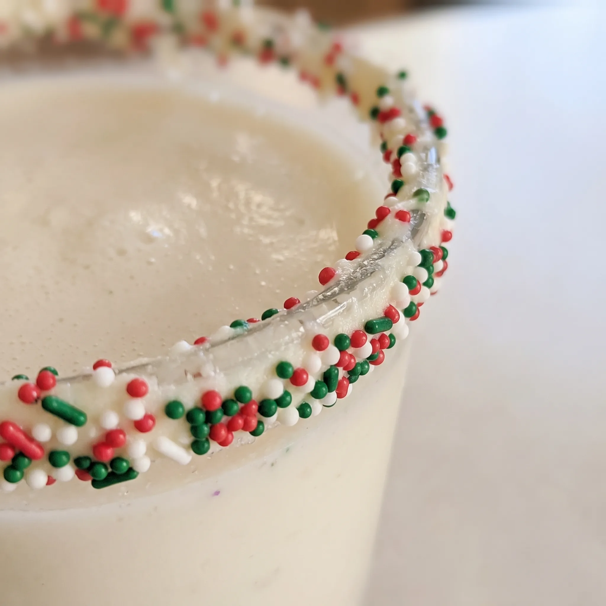 Creamy pale cocktail topped with white frosting and multicolored sprinkles along the glass edge.
